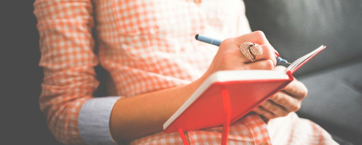 person writing on red notebook