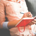 person writing on red notebook