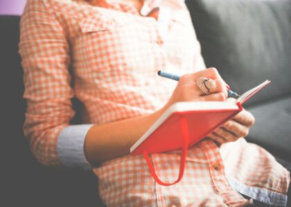 person writing on red notebook